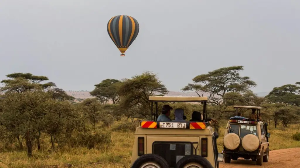 Safari vehicles in Tarangire with a Hot Air Ballon Safari in the background.